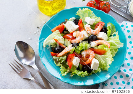 The concept of healthy and dietary food. Greek salad with shrimps and vegetables on a light stone or slate table. 97102866