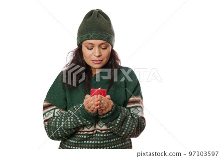 Beautiful brunette woman in warm woolen hat and sweater, looking at a fire flame of a lit candle in her hands, making wish, warming her hands, isolated on white background with copy advertising space Beautiful brunette woman in warm woolen hat and sweater, looking at a fire flame of a lit candle in her hands, making wish, warming her hands, isolated on white background with copy advertising space 97103597