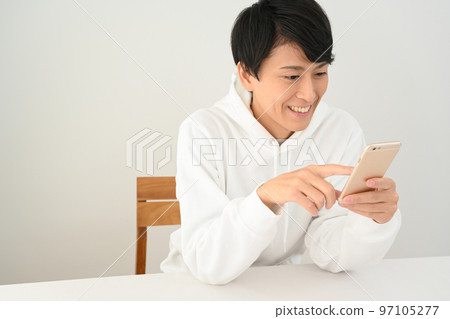 Young man operating a smartphone at a desk 97105277