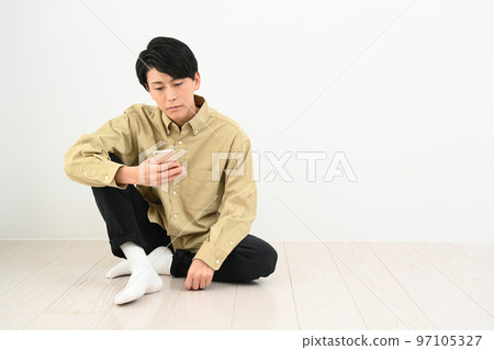 男人坐在他房間的地板上,看著他的智能手機 男人坐在他房間的地板上,看著他的智能手機 97105327