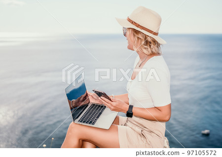 Digital nomad, Business woman working on laptop by the sea. Pretty lady typing on computer by the sea at sunset, makes a business transaction online from a distance. Freelance, remote work on vacation 97105572
