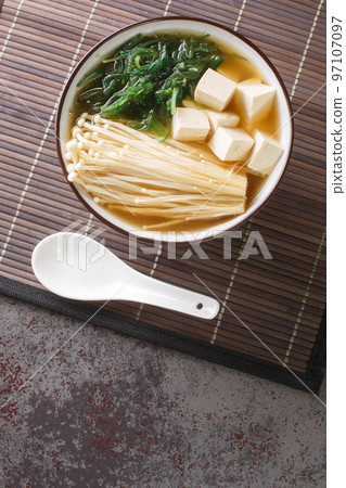 Japanese vegetarian shiro miso soup with tofu, enoki mushrooms, wakame seaweed close-up in a bowl. Vertical top view 97107097
