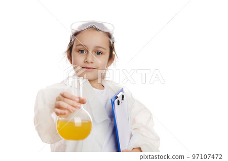 Charming smart schoolgirl in lab coat, smiles at the camera while holding out a laboratory flask with yellow liquid chemical, isolated on white background. Kids learning chemistry. Education concept Charming smart schoolgirl in lab coat, smiles at the camera while holding out a laboratory flask with yellow liquid chemical, isolated on white background. Kids learning chemistry. Education concept 97107472