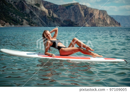 Woman sap sea. Sports girl on a surfboard in the sea on a sunny summer day. In a black bathing suit, he sits on a sapa in the sea. Rest on the sea. 97109005
