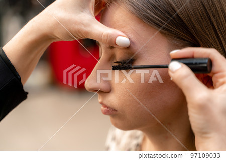 Makeup artist paints eyelashes to a woman in a beauty salon. Makeup artist paints eyelashes to a woman in a beauty salon. 97109033