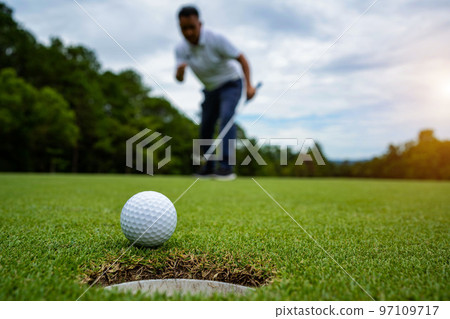 Golfer putting ball on the green golf, lens flare on sun set evening time. 97109717