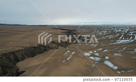A crack in the ground with a view of snowy hills 97110035