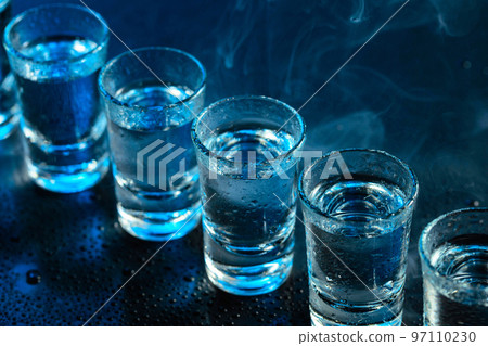 Wet glasses of vodka in smoke on dark blue background. 97110230