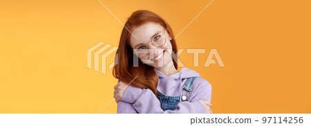 Passion, tenderness, wellbeing concept. Girl accept own self smiling charming grin tilt head hugging herself embracing body feel happiness delighted relaxing, flirty gaze camera orange background 97114256