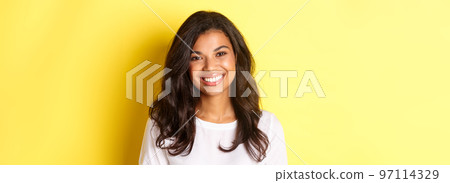 Close-up of attractive african-american woman, smiling and looking happy, standing over yellow background Close-up of attractive african-american woman, smiling and looking happy, standing over yellow background 97114329