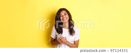Portrait of beautiful african-american woman, smiling happy and holding smartphone, standing over yellow background Portrait of beautiful african-american woman, smiling happy and holding smartphone, standing over yellow background 97114331