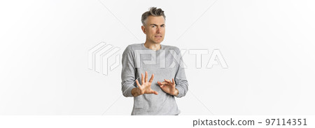 Portrait of reluctant middle-aged man avoiding something bad, shaking hands and declining offer, grimacing from disgust, standing over white background 97114351