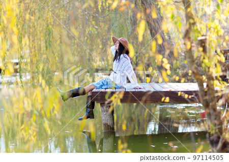 Autumn lake woman. She sits by a pond on a wooden pier in autumn and admires nature. The concept of tourism, weekends outside the city. 97114505