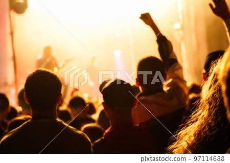Defocus cheering crowd and stage lights with space for your text. Silhouette of people raise hand up in music concert with black and yellow color spotlight on stage background. Out of focus Defocus cheering crowd and stage lights with space for your text. Silhouette of people raise hand up in music concert with black and yellow color spotlight on stage background. Out of focus 97114688