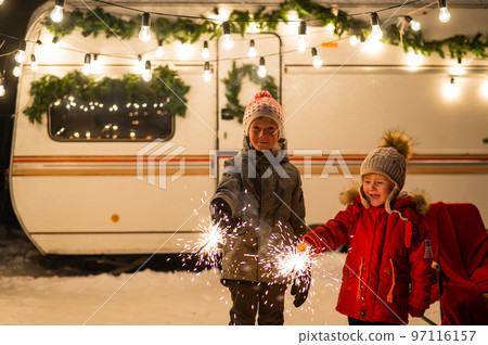 Caucasian red-haired boys hold sparklers by the trailer. Two brothers are celebrating Christmas on a trip. 97116157