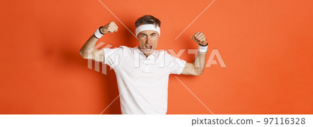 Image of funny middle-aged sportsman in white headband and t-shirt, flexing biceps to show-off, standing against orange background Image of funny middle-aged sportsman in white headband and t-shirt, flexing biceps to show-off, standing against orange background 97116328