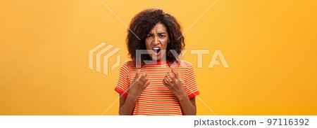 Waist-up shot of woman feeling upset feeling unfair things happened complaining and whining with regret frowning gesturing with palms near breast standing over orange background 97116392