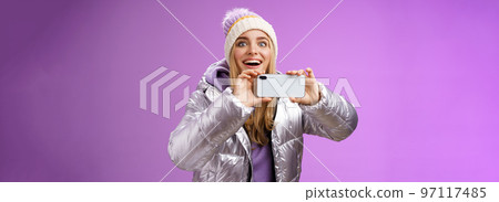 Amused fascinated female in silver jacket head smiling astonished excited look forward holding smartphone recording video taking shots famous person mobile phone camera, purple background Amused fascinated female in silver jacket head smiling astonished excited look forward holding smartphone recording video taking shots famous person mobile phone camera, purple background 97117485