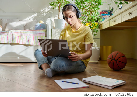 Teenage girl with headphones studying at home using a laptop Teenage girl with headphones studying at home using a laptop 97123692