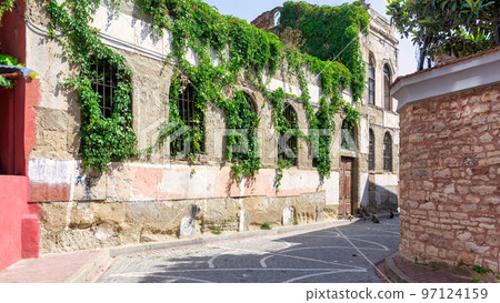 Old abandoned building, with stone wall, and wrought iron windows, covered with climber plants, in cobblestone alley Old abandoned building, with stone wall, and wrought iron windows, covered with climber plants, in cobblestone alley 97124159