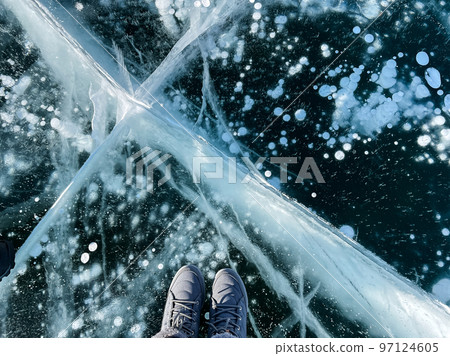 Fragile thin brittle ice underfoot. Female feet on ice. Woman wearing winter shoes 97124605