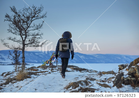 Young man standing in winter frozen nature and watching calm winter misty sunset 97126323