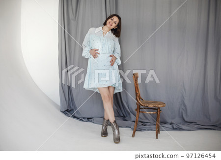 Attractive pregnant woman in white dress by the wooden chair on blue background 97126454