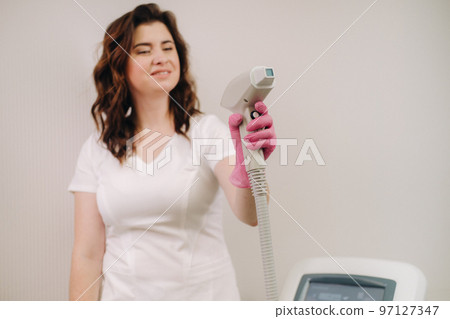 Portrait of the master of laser hair removal. A woman in a white coat holds a laser hair removal device in her hands 97127347