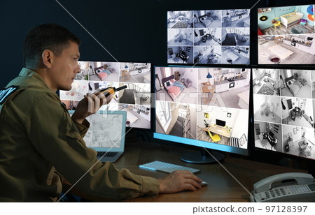 Security guard with portable transmitter monitoring modern CCTV cameras indoors 97128397