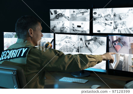 Security guard with portable transmitter monitoring modern CCTV cameras indoors Security guard with portable transmitter monitoring modern CCTV cameras indoors 97128399
