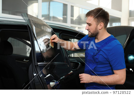 Worker tinting car window with foil in workshop Worker tinting car window with foil in workshop 97128522