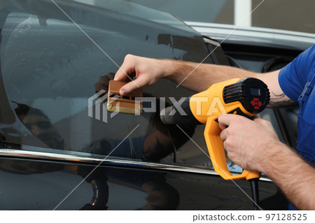 Worker tinting car window with heat gun in workshop, closeup Worker tinting car window with heat gun in workshop, closeup 97128525