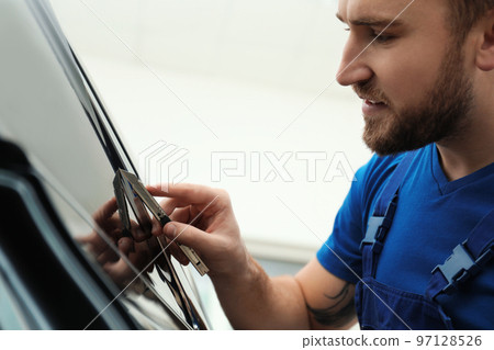 Worker tinting car window with foil in workshop Worker tinting car window with foil in workshop 97128526