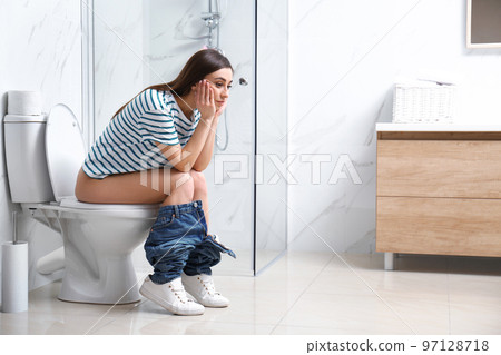 Upset woman sitting on toilet bowl in bathroom 97128718