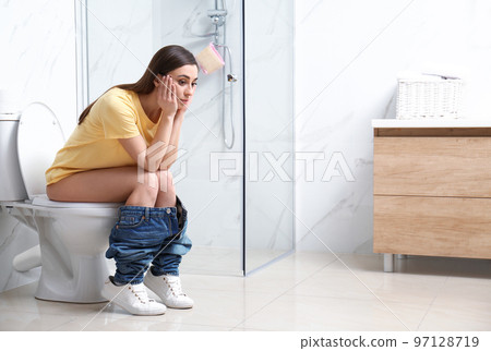 Upset woman sitting on toilet bowl in bathroom Upset woman sitting on toilet bowl in bathroom 97128719