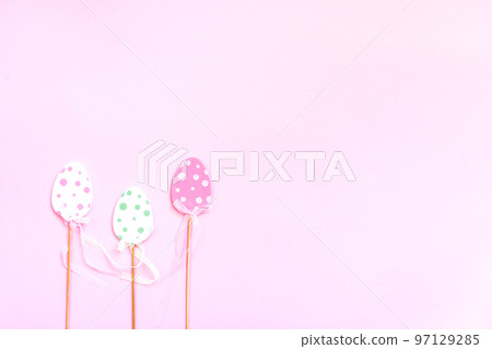Easter composition with traditional decor. Small decorative colorful eggs on wooden sticks on soft pink background. 97129285