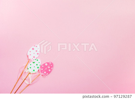 Easter composition with traditional decor. Small decorative colorful eggs on wooden sticks on soft pink background. Easter composition with traditional decor. Small decorative colorful eggs on wooden sticks on soft pink background. 97129287