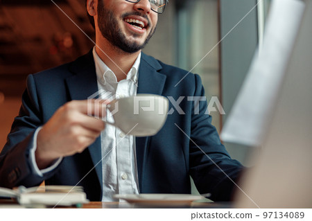 Close up of smiling unrecognisable businessman drinking coffee and working laptop in cafe 97134089