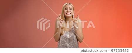 Nervous hopeful blond young woman in silver trendy dress close eyes grimacing eager wish come true cross fingers good luck praying supplicating anticiapting fortune, standing worried red background Nervous hopeful blond young woman in silver trendy dress close eyes grimacing eager wish come true cross fingers good luck praying supplicating anticiapting fortune, standing worried red background 97135452