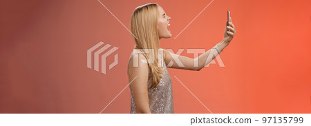 Profile shot funny carefree blond woman hold smartphone raised open mouth wide yelling recording video own shout scream, standing silver glamour dress near red background fool around Profile shot funny carefree blond woman hold smartphone raised open mouth wide yelling recording video own shout scream, standing silver glamour dress near red background fool around 97135799