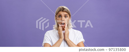 Waist-up shot of worried and shocked woman expressing empathy frowning holding hands near opened mouth feeling sorry and nervous hearing terrible disaster happened standing over purple wall Waist-up shot of worried and shocked woman expressing empathy frowning holding hands near opened mouth feeling sorry and nervous hearing terrible disaster happened standing over purple wall 97135800