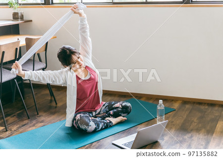 Asian woman doing light exercise stretching and yoga using a towel in the living room at home Asian woman doing light exercise stretching and yoga using a towel in the living room at home 97135882