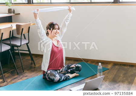 亞洲女性在家裡的客廳裡用毛巾和電腦進行康復、靈活鍛煉和瑜伽 97135884