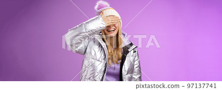 Happy relaxed smiling attractive young blond woman in stylish warm silver jacket hat hide eyes behind palm laughing happily waiting boyfriend prepared surprise gift amused, standing purple background Happy relaxed smiling attractive young blond woman in stylish warm silver jacket hat hide eyes behind palm laughing happily waiting boyfriend prepared surprise gift amused, standing purple background 97137741
