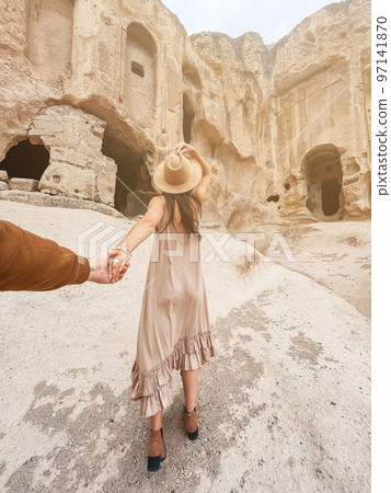 Happy young woman on background of ancient cave formations in Cappadocia, Turkey. The Monastery is one of the largest religious buildings. 97141870