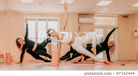 Middle aged well looking women, performing fascia exercises on the floor using a massage foam roller - tool to relieve tension in the back and relieve muscle pain. Female fitness yoga routine concept Middle aged well looking women, performing fascia exercises on the floor using a massage foam roller - tool to relieve tension in the back and relieve muscle pain. Female fitness yoga routine concept 97142444
