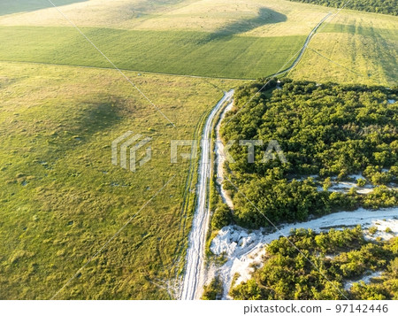 Aerial view on green wheat field and road in countryside. Field of wheat blowing in the wind on sunset. Young and green Spikelets. Ears of barley crop in nature. Agronomy, industry and food production Aerial view on green wheat field and road in countryside. Field of wheat blowing in the wind on sunset. Young and green Spikelets. Ears of barley crop in nature. Agronomy, industry and food production 97142446