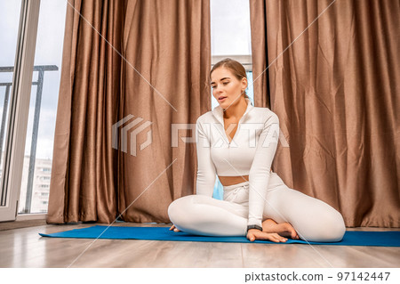 Well looking middle aged woman with long hair, fitness instructor in white sportswear, doing stretching and pilates on yoga mat at home. Healthy lifestyle, harmony, fitness yoga and meditation. Well looking middle aged woman with long hair, fitness instructor in white sportswear, doing stretching and pilates on yoga mat at home. Healthy lifestyle, harmony, fitness yoga and meditation. 97142447