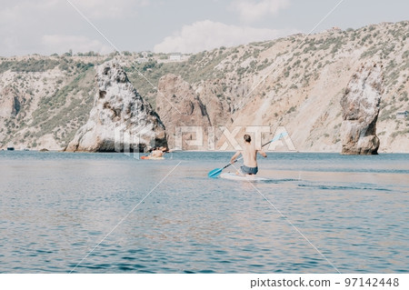 Side view foto of a man swiming and relaxing on the sup board. Sportive man in the sea on the Stand Up Paddle Board SUP. The concept of an active and healthy life in harmony with nature. Side view foto of a man swiming and relaxing on the sup board. Sportive man in the sea on the Stand Up Paddle Board SUP. The concept of an active and healthy life in harmony with nature. 97142448