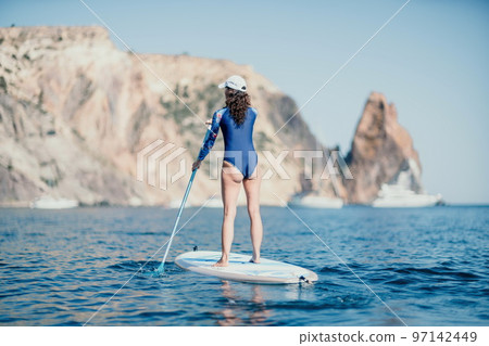 Woman sup yoga. Middle age sporty woman practising yoga pilates on paddle sup surfboard. Female stretching doing workout on sea water. Modern individual female hipster outdoor summer sport activity. Woman sup yoga. Middle age sporty woman practising yoga pilates on paddle sup surfboard. Female stretching doing workout on sea water. Modern individual female hipster outdoor summer sport activity. 97142449